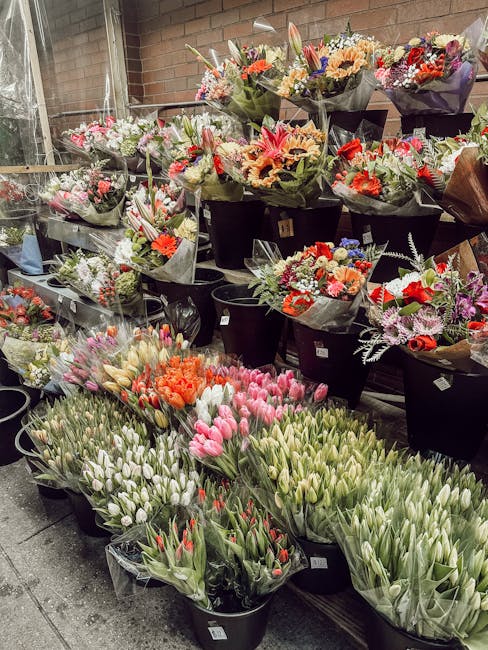 An assortment of fresh bouquet arrangements and floral displays at a florist shop, featuring a variety of flowers including pink tulips, orange tulips, white tulips, and purple statice, arranged in bl
