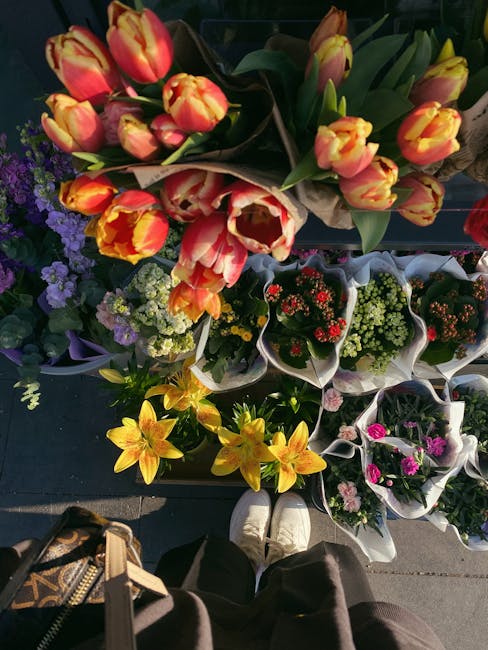 A display of fresh flower bouquets arranged outdoors, featuring a variety of vibrant blooms including yellow lilies, pink and yellow tulips, purple and white statice, and small red and white flowering